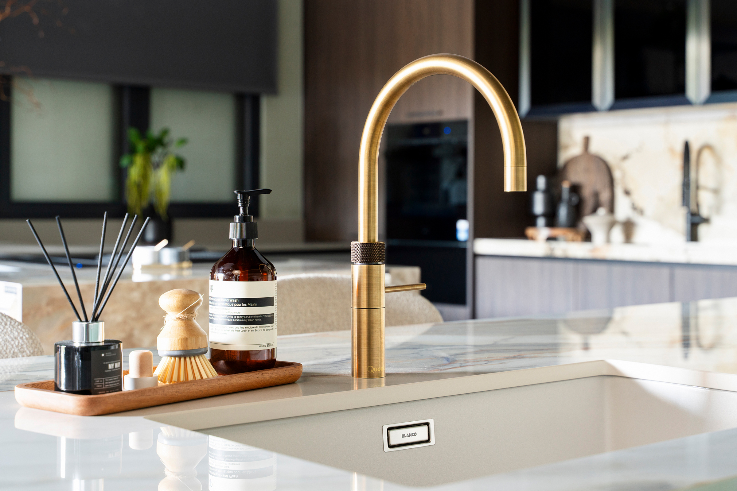 Close-up of patinated brass Quooker tap on marble-effect quartz worktop, designed by KCA to showcase luxury detailing and refined functionality in trade kitchens.