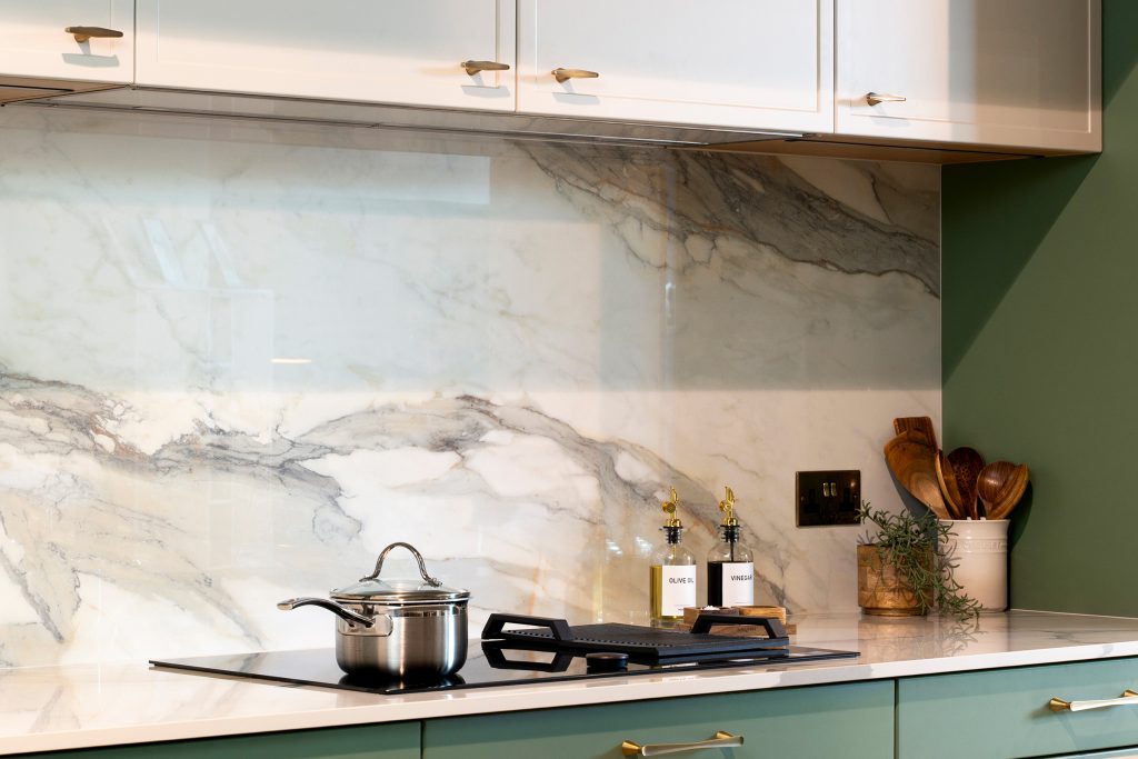 Close-up of KCA’s two-tone trade kitchen featuring marble-effect quartz splashback, integrated induction hob and brass detailing — showcasing precision engineering and refined modern design.
