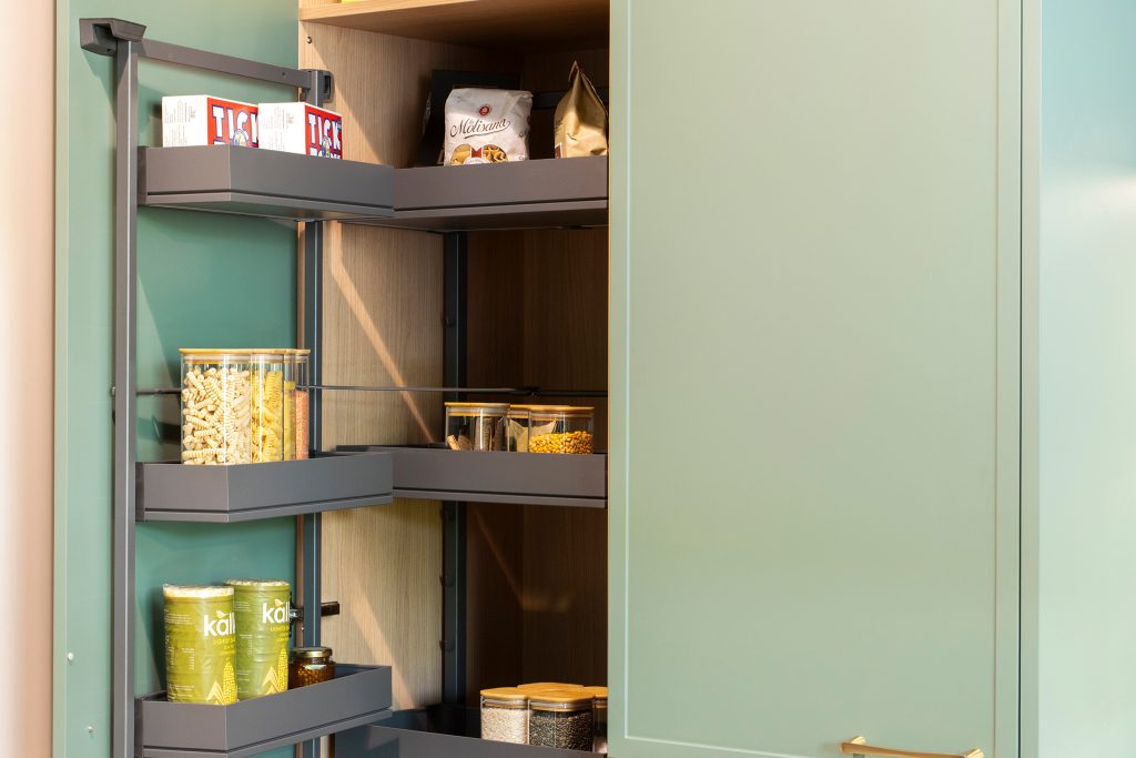 Pull-out pantry unit in Eucalyptus Green trade kitchen by KCA, featuring internal oak shelving and intelligent storage design for modern developments.